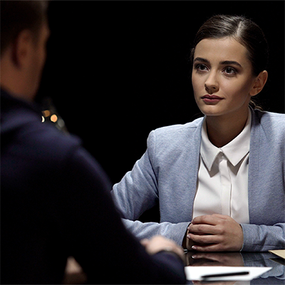 Woman conducting an interrogation of a man whose back is to the camera.